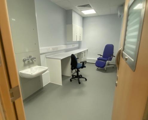 A room with a door, blue chair, black chair, sink and desk