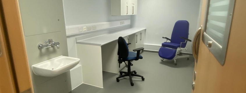 A room with a door, blue chair, black chair, sink and desk